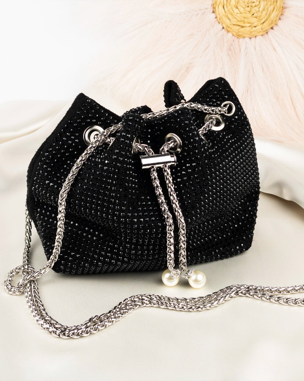 Black rhinestone-decorated bucket bag with a chain strap and drawstring closure, displayed on a flat surface.