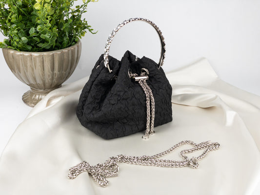 Black textured handbag with chain handle on a white surface with a plant in the background