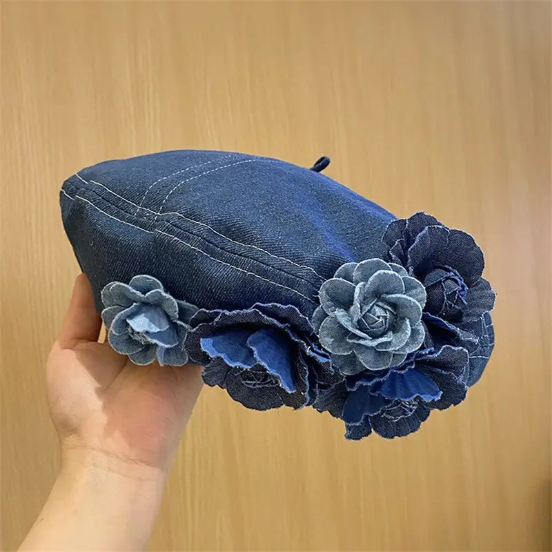 Blue denim beret with floral decorations held against a wooden background