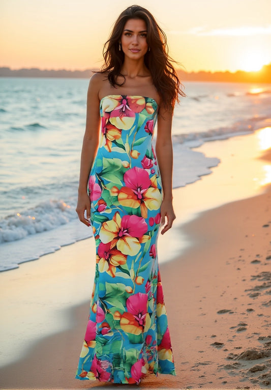 Woman in a colorful floral dress standing on a beach at sunset.