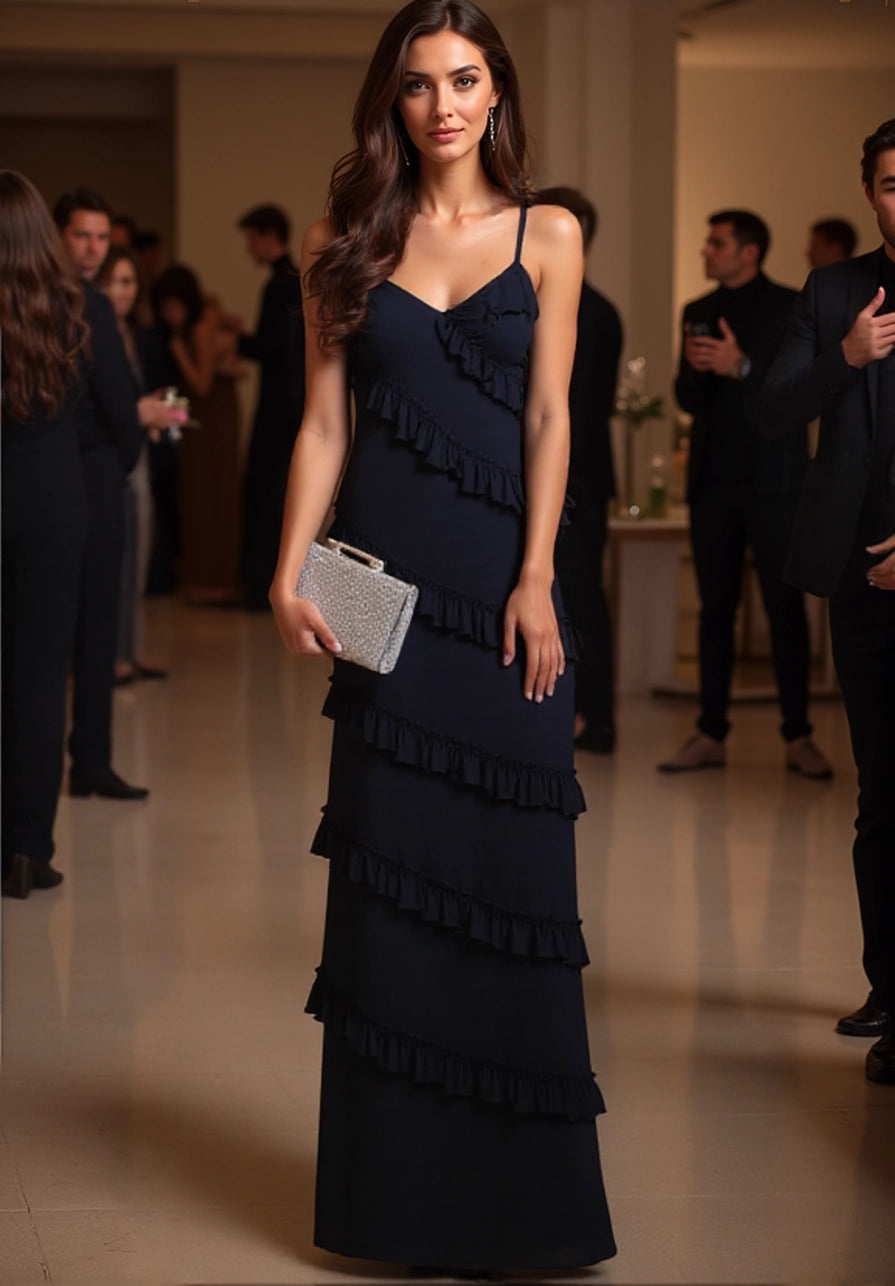 Woman in a dark blue ruffled dress holding a clutch in an indoor setting with people around.