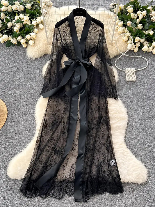 Black lace robe with satin ribbon on a white fur surface with floral decorations.